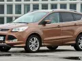 Brązowy Ford Kuga 2019 z kierowcą w okularach, zaparkowany na mokrym parkingu przed nowoczesnym budynkiem.