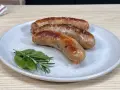 Tre salsicce dorate e succulente, appena cotte in padella, riposano su un piatto con rametti di rosmarino e alloro.