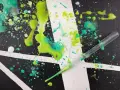 Projection de peinture sur toile, avec des éclaboussures vertes et turquoise sur un fond noir et blanc. Une pipette est visible, prête à projeter plus de peinture.