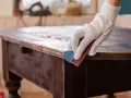 Mano guantata leviga un tavolo antico, un'idea per trasformare mobili antichi in moderni con un tocco di fai-da-te.