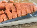 Pokrojony łosoś, idealny jaki łosoś do sushi, leży na desce obok noża.