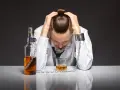 Mężczyzna w kajdanach, przykuty łańcuchem do butelki i szklanki z alkoholem. To symbol zniewolenia przez grupę alkoholową.