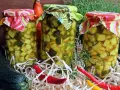 Słoiki z cukinią w zalewie słodko-kwaśnej z curry, ozdobione kolorowymi materiałami. Obok leżą świeże cukinie i papryczki chili.
