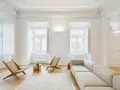 Ecco cosa fa l'architetto d'interni: crea un soggiorno minimalista con divano chiaro, sedie in legno e un tavolino dorato, valorizzando la luce naturale.