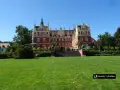 Majestatyczny pałac w parku muzakowskim, otoczony zielonym trawnikiem i drzewami, pod błękitnym niebem.
