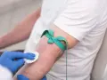 Ręka pacjenta z opaską uciskową i wacikiem, przygotowywana do pobrania krwi.