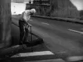 Une photo dans la rue : un vieil homme se penche sur sa canne, le regard perdu, au bord d'une route déserte.