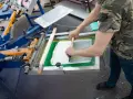 Proceso de serigrafía que es: un operario aplica tinta blanca sobre una pantalla para estampar.