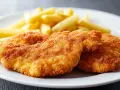 Due cotolette di pollo dorate e croccanti, accompagnate da patatine fritte, su un piatto bianco.