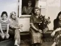 Maria Wojewodzka z rodziną na tle domu. Kobiety w różnym wieku, jedna z nich trzyma kwiaty.