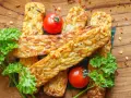 Złocisty, smażony tempeh, czyli co to jest? Podany z pomidorkami i natką pietruszki na drewnianej desce.