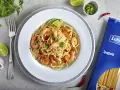 Pyszny makaron z krewetkami na winie, udekorowany limonką i natką pietruszki. Obok opakowanie makaronu spaghetti Lubella.