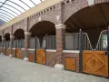 Belle écurie pour chevaux avec des boxes en briques rouges, des portes en bois et un toit transparent.