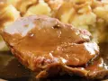 Mięciutka karkówka w sosie, podana z purée ziemniaczanym. Danie wygląda apetycznie i soczyście.