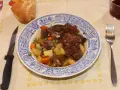 Un plato de corzo guisado con patatas, zanahorias y guisantes, acompañado de pan y vino tinto. ¡Una de las mejores recetas de corzo guisado!