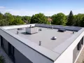 Nowoczesny dach płaski bez attyki z systemem wentylacji i klimatyzacji, otoczony zielenią.