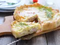 Una fetta di torta salata prosciutto e formaggio, guarnita con aneto, su un tagliere di legno.