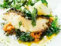 Delicioso bacalao al pil pil, con su piel dorada, acompañado de verduras frescas y una salsa vibrante.