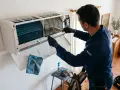 Técnico realiza revisión de aire acondicionado, limpiando filtros con cepillo.