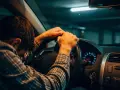 Mann mit Kopf auf Lenkrad, verzweifelt. Fahren ohne Versicherungsschutz strafe droht. Dunkle Garage, gedämpftes Licht.