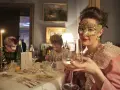 Elegancka kobieta w złotej masce i perłach świętuje karnawał 2026. Wznosi kieliszek wina, otoczona innymi gośćmi w maskach.