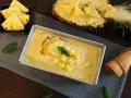 Erfrischendes Ananas Eis in einer Metallform, garniert mit Ananasstücken und Minze. Daneben liegen Ananasspalten und eine Waffel.
