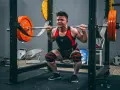 En person utför squats med vikt i ett gym.