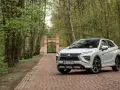 Biały Mitsubishi Eclipse Cross na tle bramy i drzew. Wiele pozytywnych mitsubishi eclipse cross opinie potwierdza jego wszechstronność.