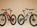 Two full-suspension mountain bikes, one orange and maroon, the other grey, are displayed side-by-side, showcasing the 27.5 vs 29 wheel size debate.