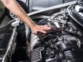 Mano che pulisce il motore dell'auto con un panno scuro, parte di un lavaggio motore accurato.