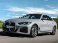 Eleganckie, szare BMW Gran Coupé sunie po drodze na tle błękitnego nieba z chmurami.