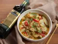Un tazón de patatas a lo pobre, con pimientos rojos y verdes, perejil picado y una botella de aceite de oliva virgen extra.