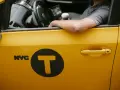 Kierowca żółtej taksówki NYC z logo "T" w kole. Zastanawiasz się, ile zarabia taksówkarz w tym mieście?