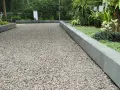 Un chemin de gravier cours maison, bordé de pierres grises et de verdure luxuriante, invite à la promenade.