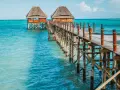 Drewniany pomost prowadzi do chat na palach nad turkusową wodą. Zanzibar, pora deszczowa, ale słońce świeci.