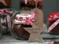 Burkar med ingredienser för varm choklad jul, dekorerade med röda band och pepparkaksfigurer. En stjärna med texten "Julens varma choklad" hänger framför.
