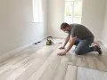 Mężczyzna w masce zakłada jasny panel winylowy, tworząc nowoczesną podłogę.