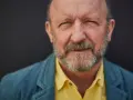 Artur Barciś w żółtej koszuli i niebieskiej marynarce, z siwą brodą, patrzy w obiektyw.