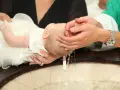 Chrzest dziecka. Woda spływa z rąk księdza do chrzcielnicy. Zastanawiasz się, ile daje się na chrzciny?