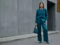 Kobieta w eleganckim, futrzanym swetrze i satynowych spodniach w kolorze petrol. Torebka i buty również w tym samym odcieniu.