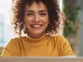 Lächelnde Frau mit Locken am Laptop, bereit für ihre Bewerbung als studentische Hilfskraft.