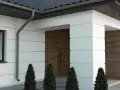 Nowoczesny dom z białymi boniami, drewnianymi drzwiami i dachówką.