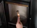 Mano con pennello per pulire il vetro della stufa bruciato.