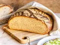 Frisches Brot mit knuspriger Kruste, bereit, mit Wasser bestrichen zu werden. Daneben ein Korb mit weiteren Brotscheiben.