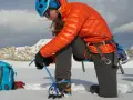 Alpinistka zakłada raki górskie na buty, przygotowując się do wspinaczki w śnieżnych górach.
