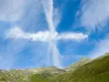Ein Kreuz aus Wolken am blauen Himmel über grünen Bergen. Man könnte sagen, ihr werdet Zeichen am Himmel sehen.