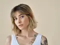Kobieta z tatuażami na ramionach i dekolcie, z modną fryzurą long bob i grzywką.