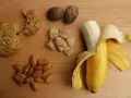 Na drewnianym blacie leżą orzechy, migdały, kawałek ciastka, kandyzowany imbir i banan. To świetne węglowodany złożone produkty.