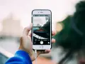 Dłoń trzyma iPhone'a, pokazując ekran z widokiem miasta. Dowiedz się, jak robic zdjecia iphonem, by uchwycić takie ujęcia.