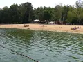 Plaża nad jeziorem Szperek, z kilkoma osobami odpoczywającymi na piasku i wodą w tle.